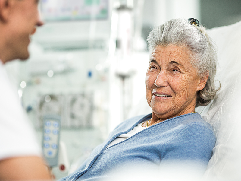 Eldery woman smiles and sitting in a bed with a raised backrest