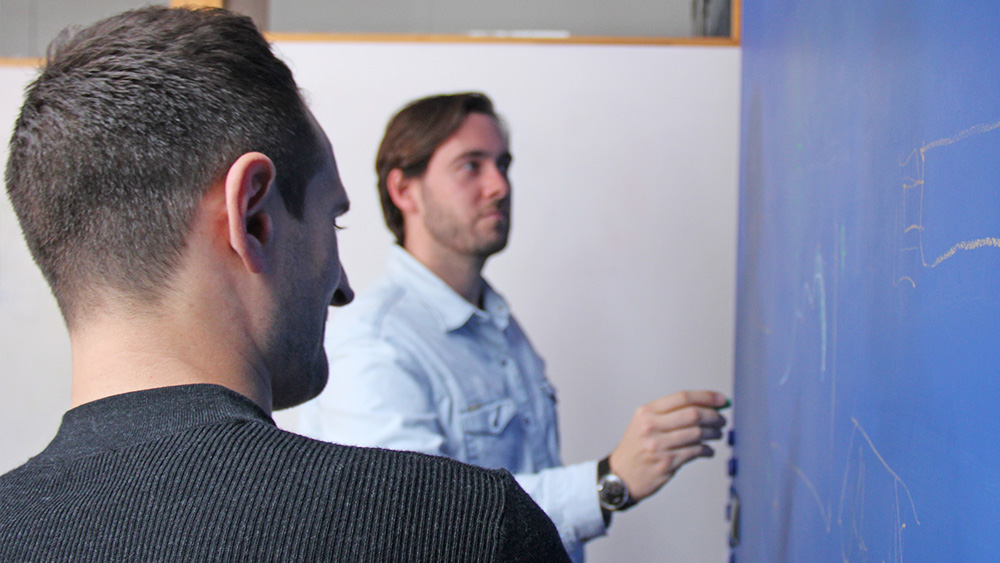 Two men stand at a blueboard and make sketches